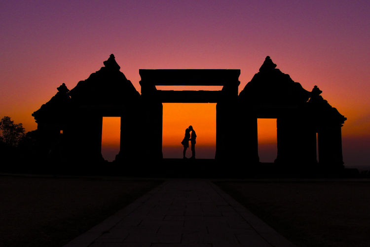 Silhouette couple kissing on gateway of ratu boko ruins against clear sky