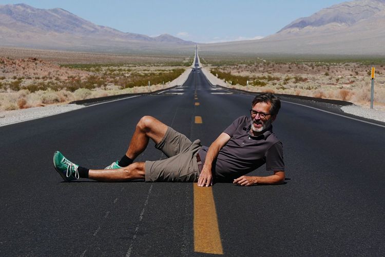 Mature man lying on road against sky