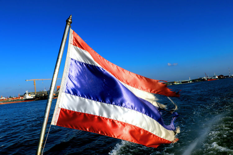Panoramic view of flag on sea against clear blue sky