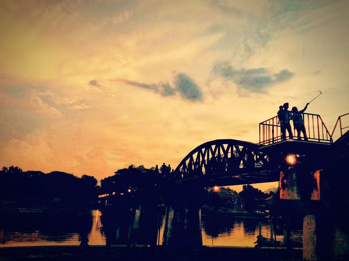Silhouette people on bridge in city against sky during sunset