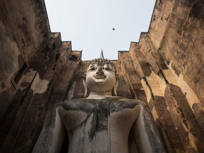 Low angle view of buddha statue on building against sky