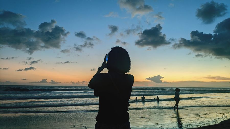 Silhouette woman standing on beach against sky during sunset