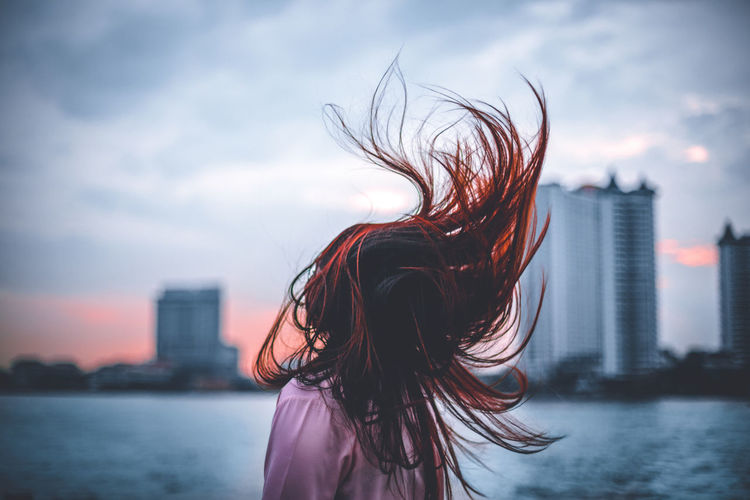 Rear view of woman tossing hair against sky in city