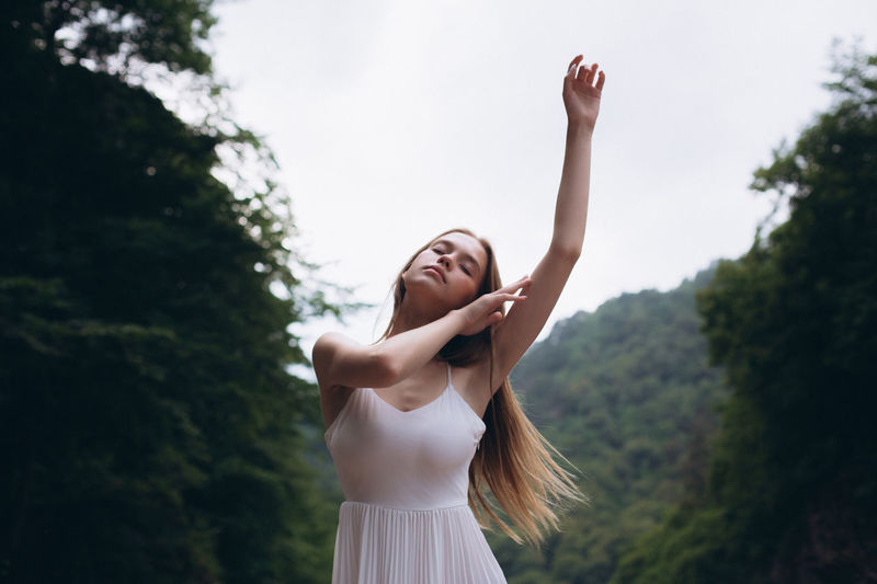 Young woman with arm raised standing against trees