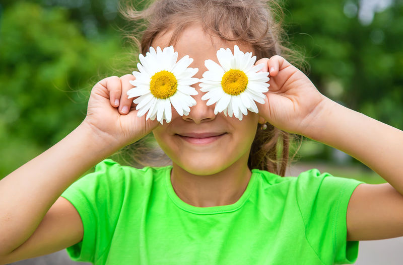 Smiling girl holding flowers in front of eyes