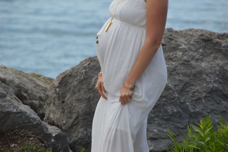 Midsection of pregnant woman standing on rock by sea
