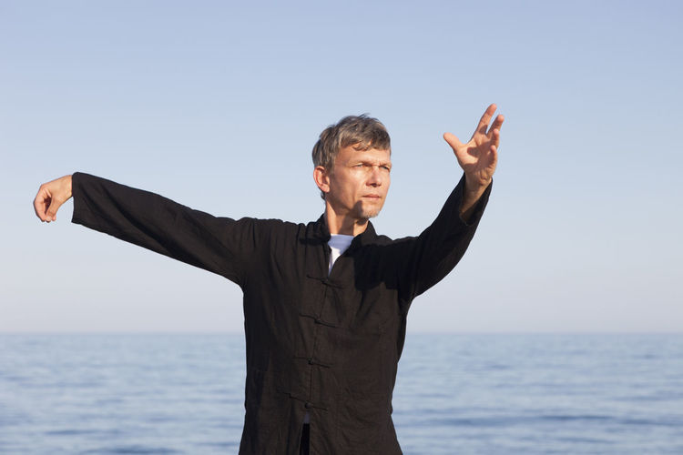 Man practicing martial arts while standing by sea against clear sky