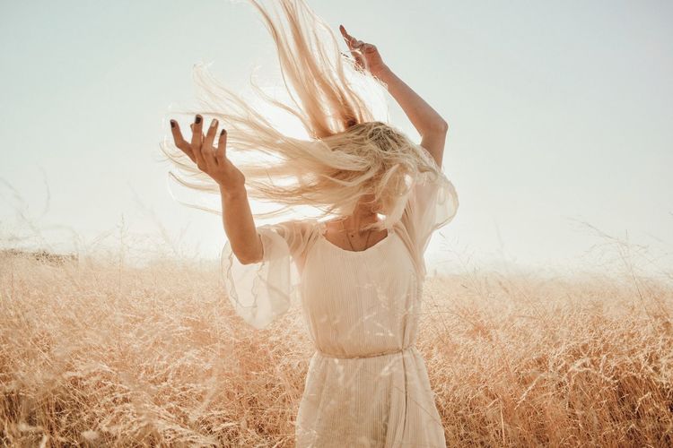 Woman tossing blond hair while standing on grassy field