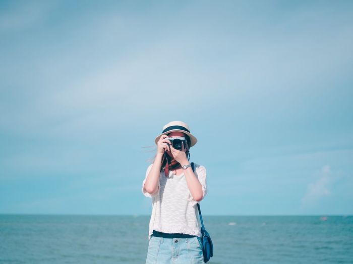 Full length of young woman photographing against sea