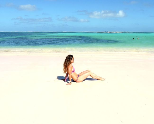 Full length of woman relaxing at beach against sky