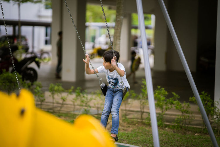Full length of boy looking away while sitting on swing in playground