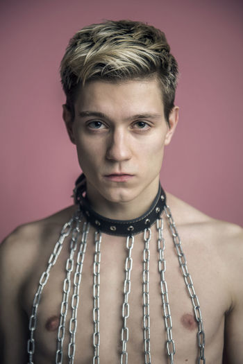 Portrait of young man wearing chain collar against pink background