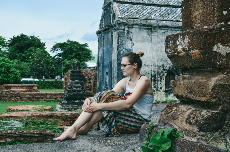 Side view of woman sitting against old built structure