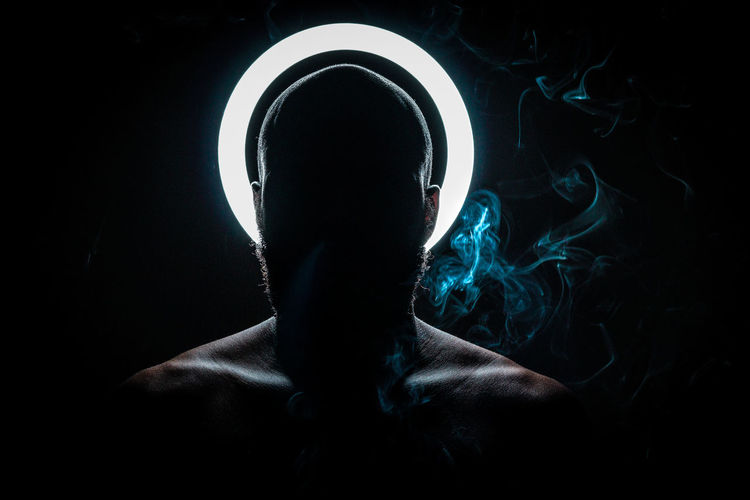 Shirtless man smoking cigarette against black background