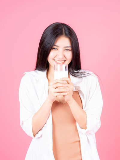 Portrait of beautiful young woman drinking glass against pink background