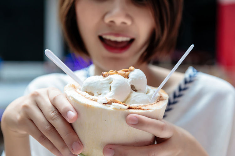 Coconut ice cream in coconut shell in woman hands enjoying eating, thailand street food