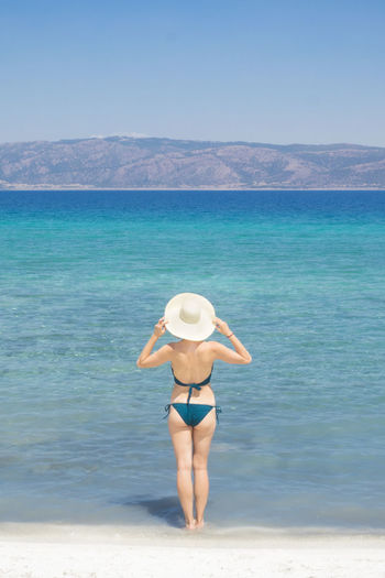 Rear view of sensuous woman wearing bikini while standing on shore at beach