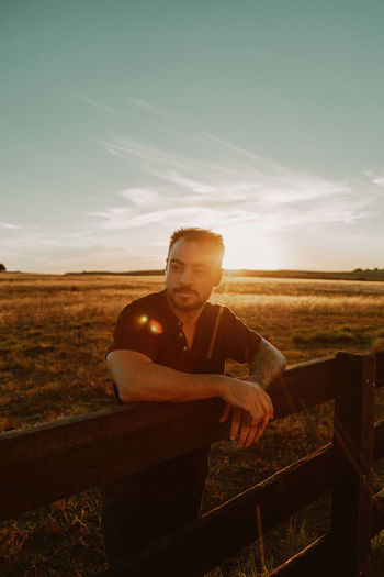 Man looking away while standing at farm during sunset