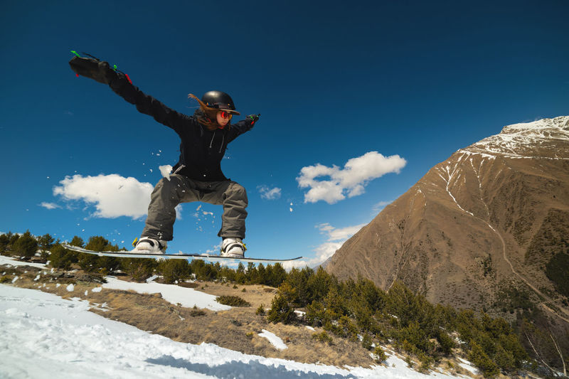 Snowboarder woman jumping from a kicker springboard from the snow on a sunny day in the mountains 