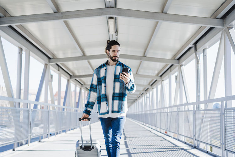 Man using mobile phone while walking with luggage on bridge