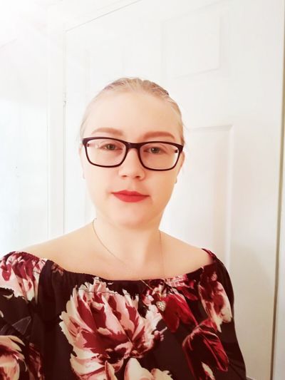 Portrait of young woman wearing eyeglasses against white door