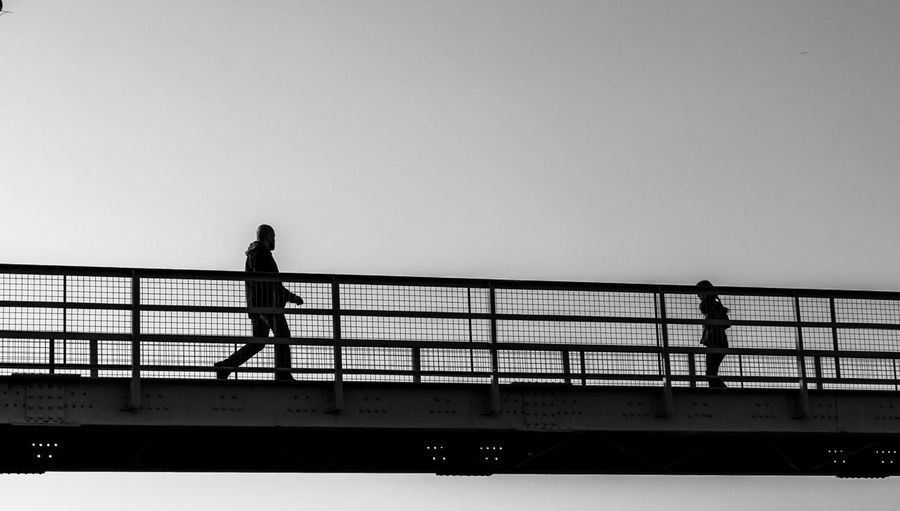 Silhouette people walking on footbridge against clear sky