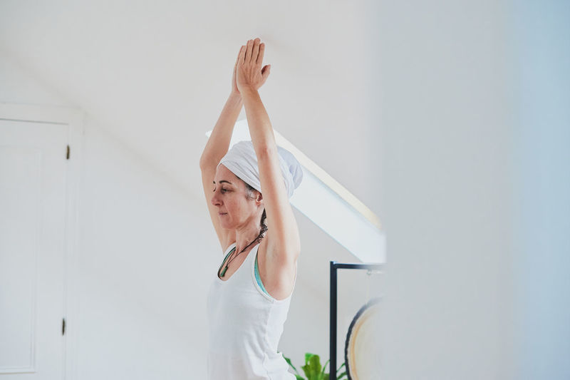 Female standing in vrksasana pose while practicing yoga on soft carpet and looking away in house room