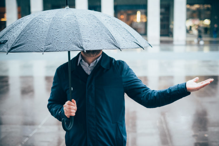Midsection of man holding umbrella in city