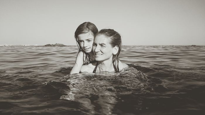 Mother carrying daughter while swimming in sea against clear sky