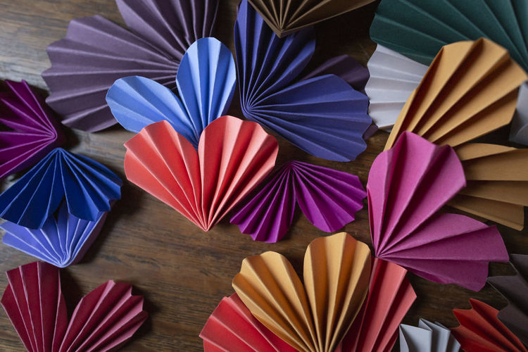 Multi-colored paper origami hearts arranged on wooden background