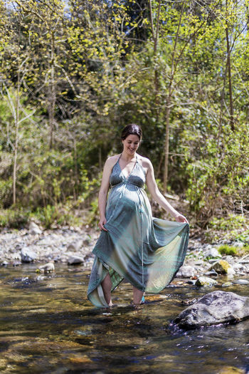 Pregnant woman standing in river at forest