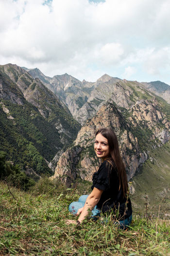 Portrait of young woman sitting against mountain range