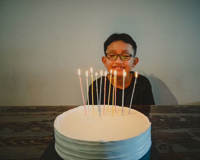 Colourful candles on white cake. a young boy is celebrating birthdays together.