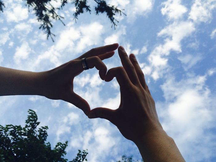 Cropped hands of couple making heart shape against blue sky