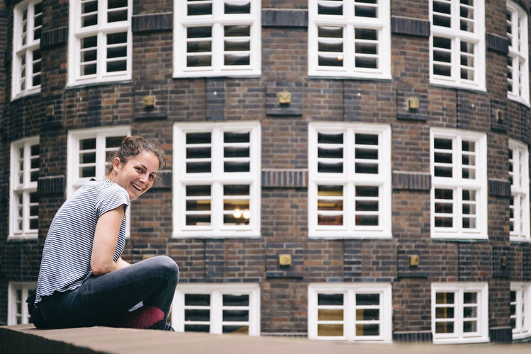 Portrait of young woman sitting on retaining wall against building