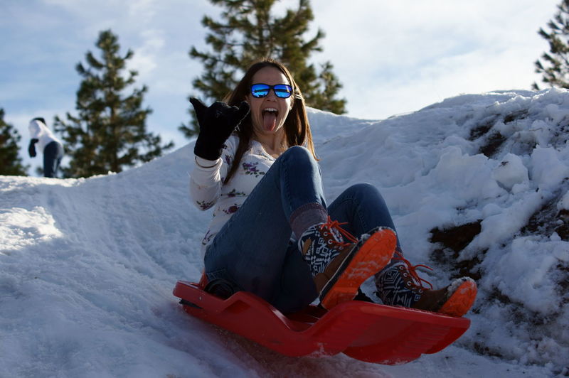 Cheerful woman sitting in sled on snow covered mountain against sky