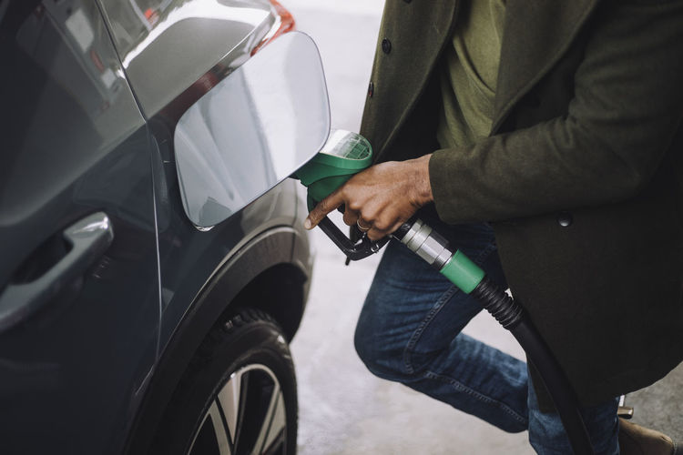 Low section of mature man refueling car while standing at gas station