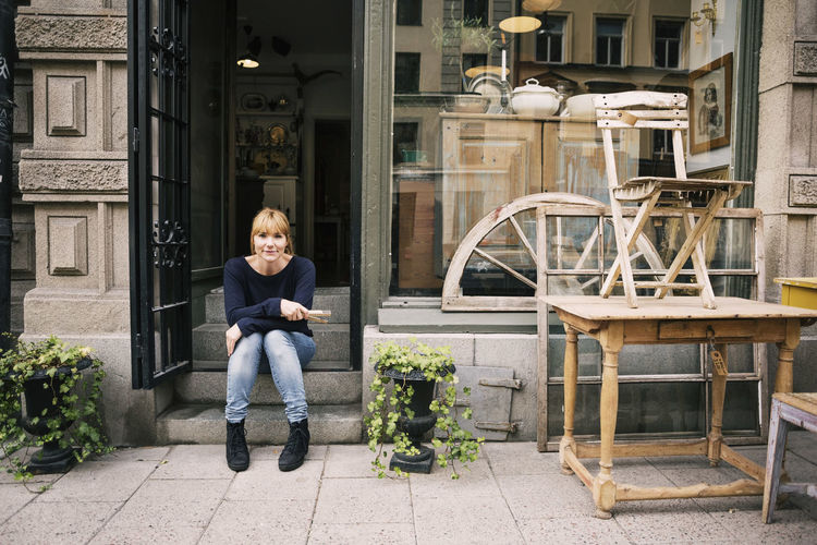 Female owner sitting on steps of antique shop