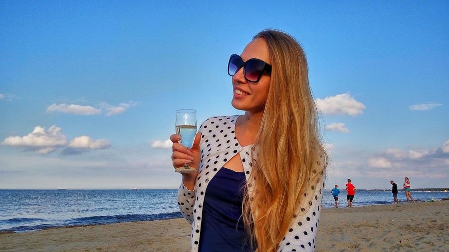 Young woman holding wineglass at sopot beach against sky