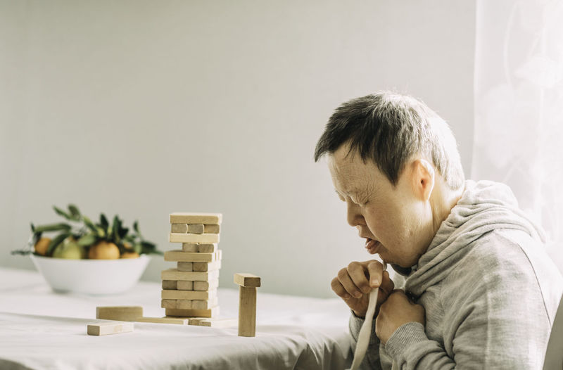 An elderly woman with down syndrome builds towers of wooden toy blocks