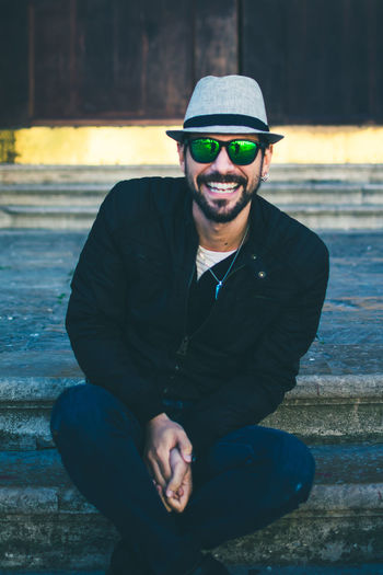 Portrait of cheerful young man wearing sunglasses while sitting on steps