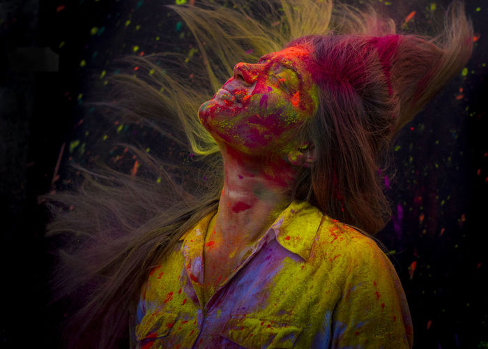 Close-up of woman with powder paint tossing hair against black background