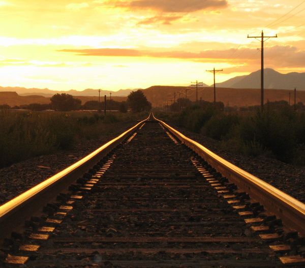 Railroad track on field against sky at sunset