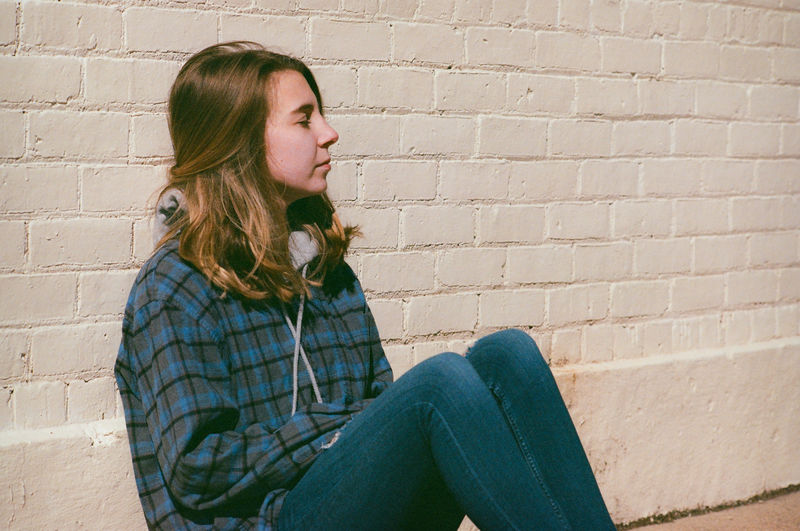 Woman looking away while sitting against brick wall