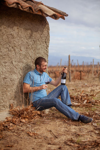 Man sitting on the ground near an old building in a vineyard and tasting wine
