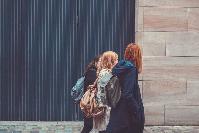 Side view of female friends walking against wall
