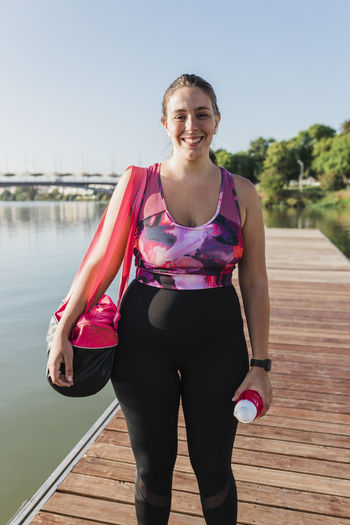 Smiling sportswoman with bag standing on pier