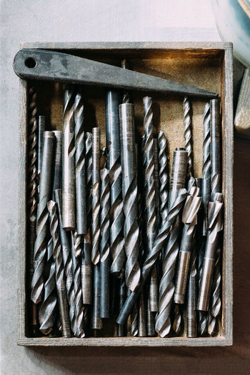 Top view collection of various metal twist drill bits in box on table in workshop