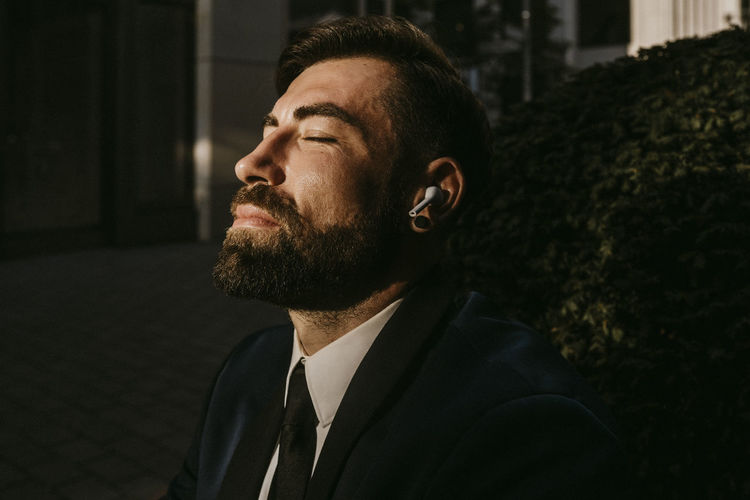 Businessman with eyes closed listening music through wireless earphones