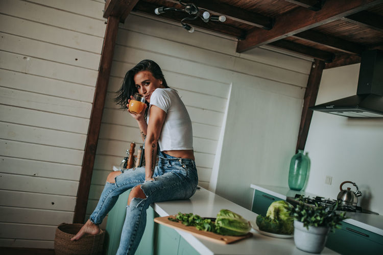 Woman drinking juice while sitting in kitchen counter